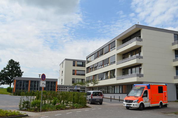 Das Foto zeigt die Frontansicht des viergeschossigen St. Rochus-Krankenhauses mit der kleinen Kapelle. Im Vordergrund steht ein Rettugswagen.