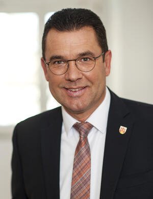 Das Foto zeigt ein Portrait des Bürgermeisters Carsten Torke im dunkelblauen Sakko und weißem Hemd mit beerenfarbenen gestreiften Krawatte.