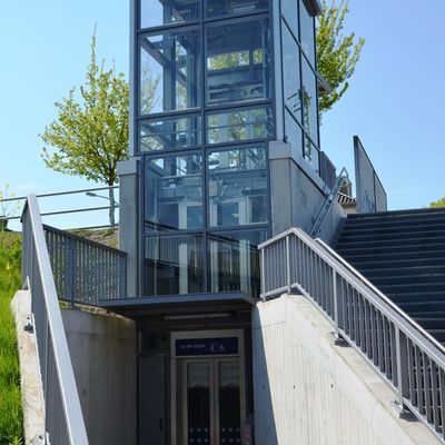 Das Foto zeigt den Fahrstuhl am Bahnhof in Steinheim von der Billerbeckerstraße aus. Die Böschung rechts und Links wird durch Betonwände abgefangen. Von dort kann man dann den Höhenunterschied zum höher gelegenen Bahnhof überbrücken.