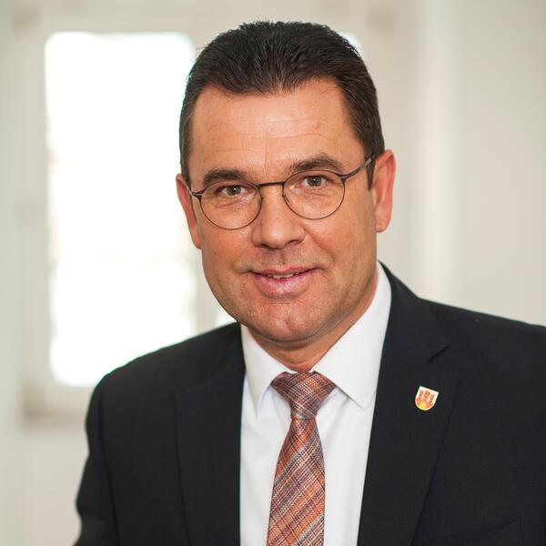 Das Foto zeigt ein Portrait des Bürgermeisters Carsten Torke im dunkelblauen Sakko und weißem Hemd mit beerenfarbenen gestreiften Krawatte.