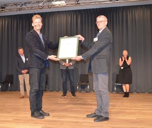 Das Foto zeigt die Übergabe des gerahmten Zertifikats durch Herrn Christian Felber an Heinz-Josef Senneka von der Stadt Steinheim.